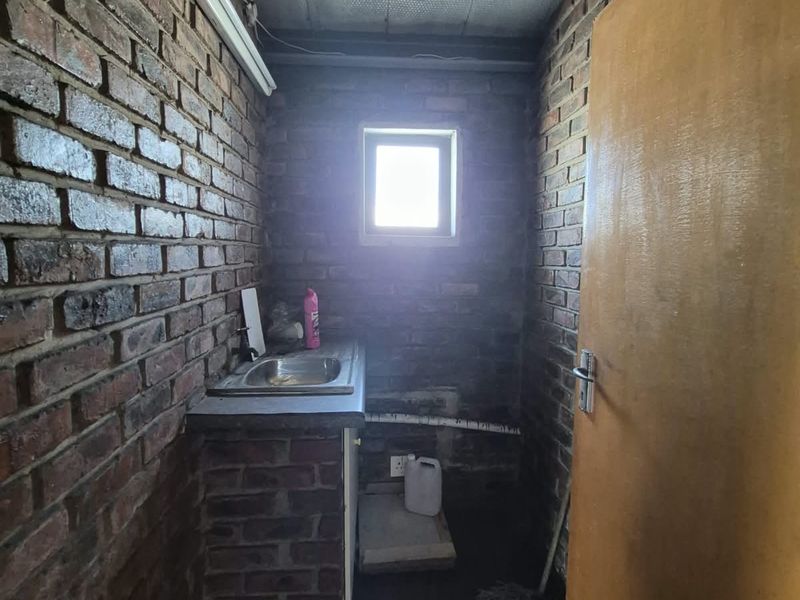 A utility space featuring exposed brick walls, a built-in sink, and a drop ceiling, offering a functional area for storage or maintenance tasks.