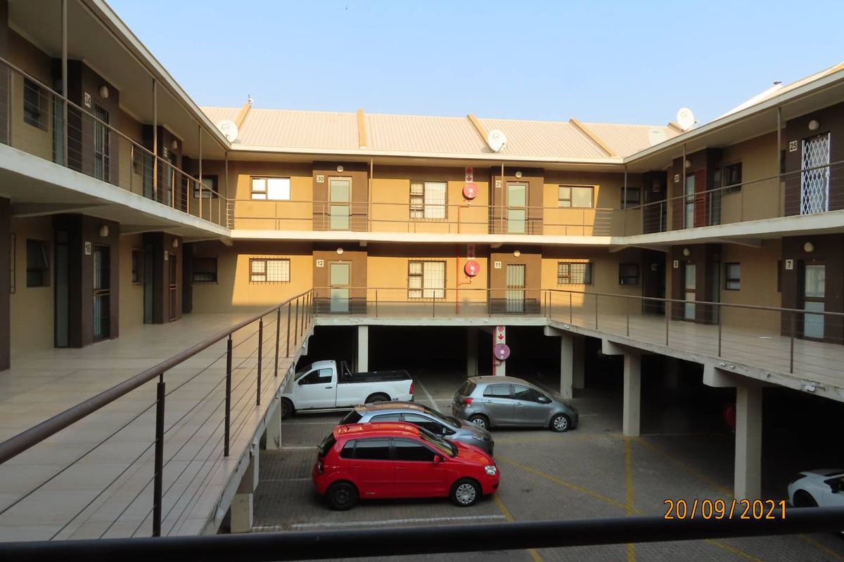 Exterior view of a multi-story apartment complex featuring open-air walkways, metal railings, and a ground-level parking area.