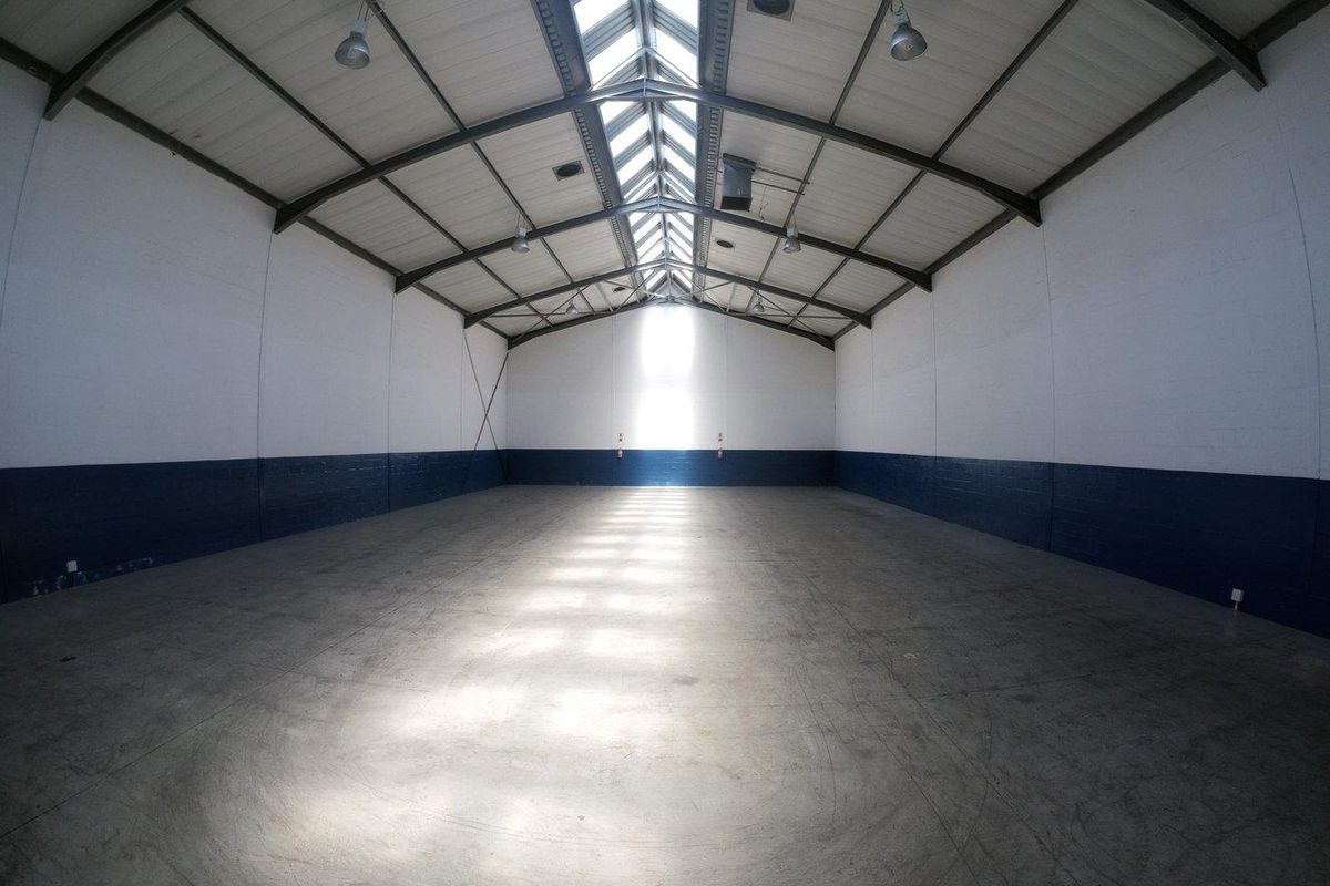 Spacious industrial warehouse unit featuring high ceilings with exposed steel trusses, a central skylight, concrete flooring, and durable painted masonry walls.