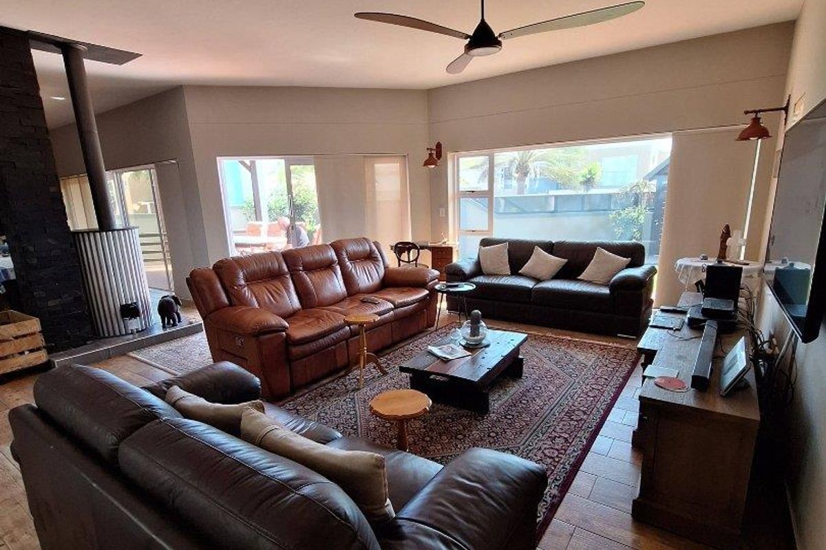 Spacious living room featuring wood-look tile flooring, a modern ceiling fan, and a prominent black stone-clad fireplace.