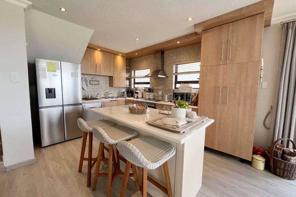 A well-appointed kitchen featuring light wood cabinetry, a central island with stone countertop, stainless steel extractor fan, and tiled backsplash.