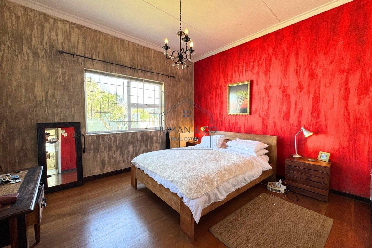 A spacious bedroom featuring wooden flooring, a decorative chandelier, and bold textured wall finishes, providing a unique character to the sleeping area.