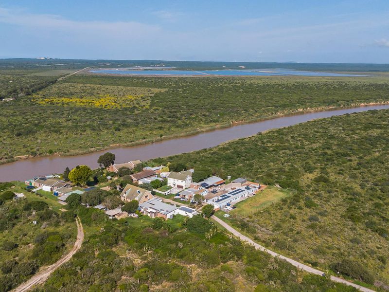 Aerial view of a rural property complex situated along a river, featuring multiple buildings with solar installations and surrounding natural landscape.