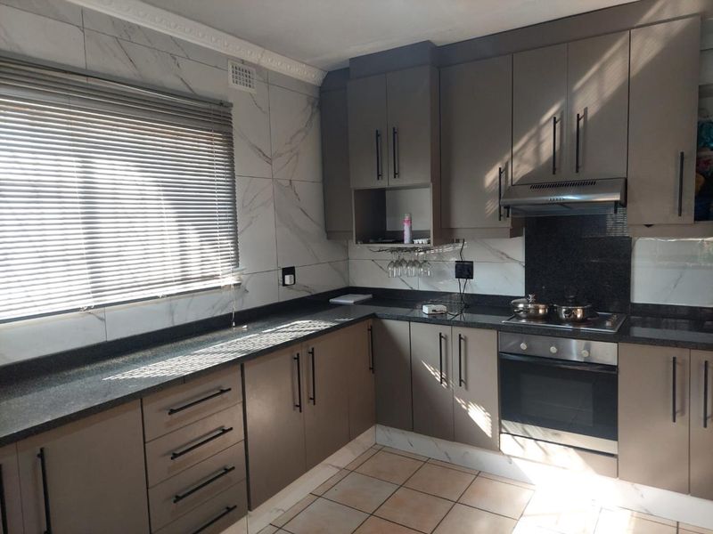 Modern kitchen featuring granite countertops, built-in oven and hob, extractor fan, and marble-look wall tiling with ample storage cabinetry.