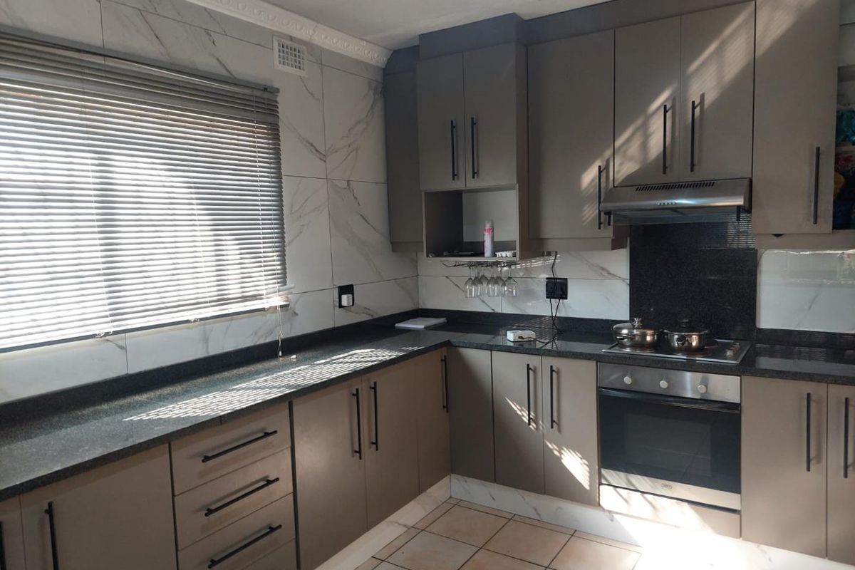 Modern kitchen featuring granite countertops, built-in oven and hob, extractor fan, and marble-look wall tiling with ample storage cabinetry.