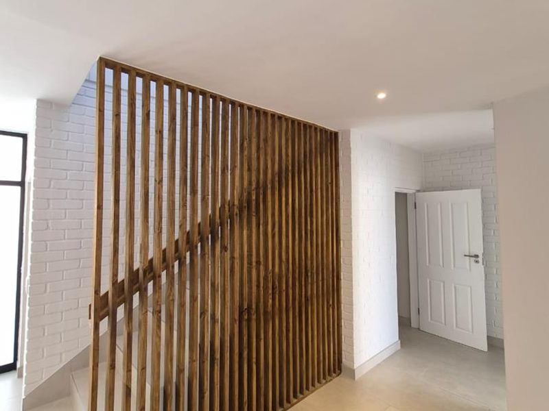 A bright, modern hallway featuring a stylish timber slat staircase screen, white painted brick walls, and neutral floor tiles.