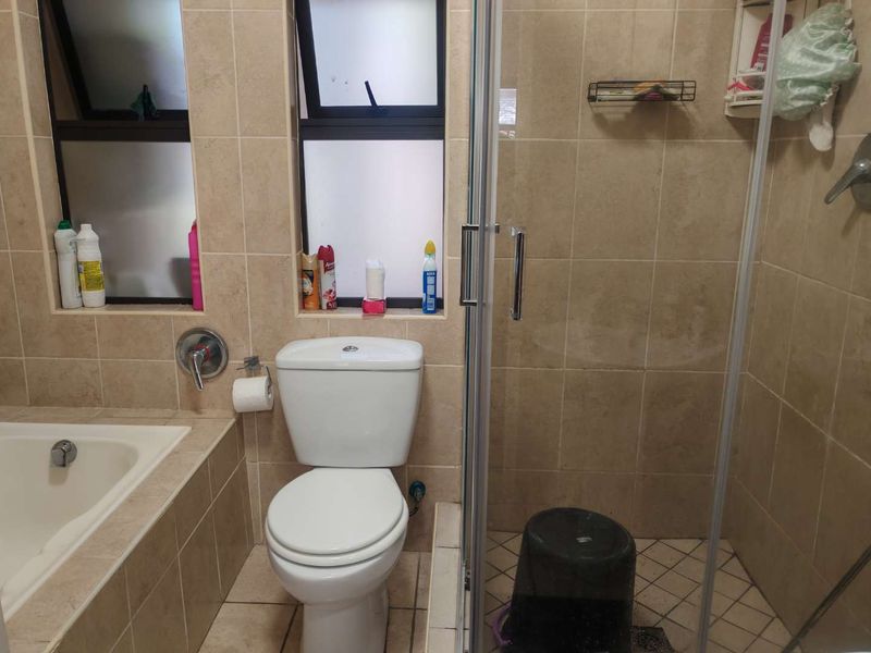 A functional bathroom featuring a built-in bathtub, a separate glass-enclosed shower, and neutral ceramic tiling throughout.