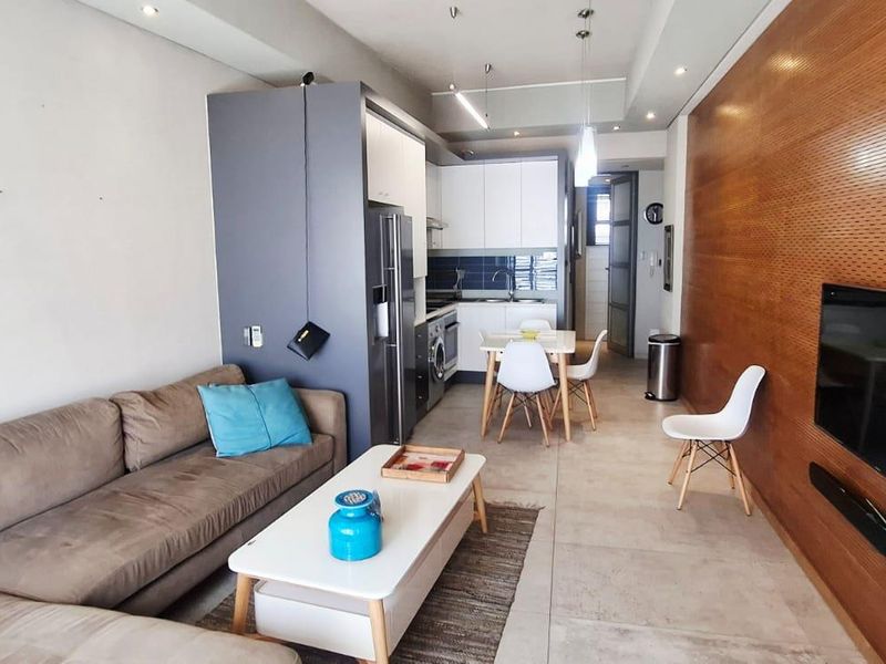 Modern open-plan apartment featuring a sleek kitchen, tiled flooring, and a striking wood-paneled feature wall, creating a cohesive and contemporary living space.