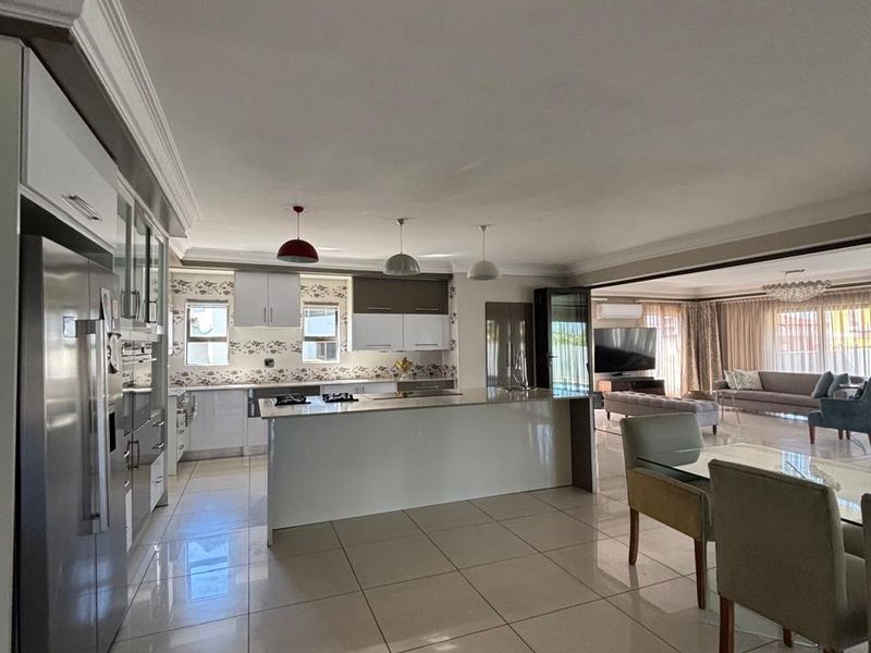 Spacious open-plan living area featuring a modern kitchen with a central island, sleek cabinetry, and large format floor tiles flowing into the lounge.