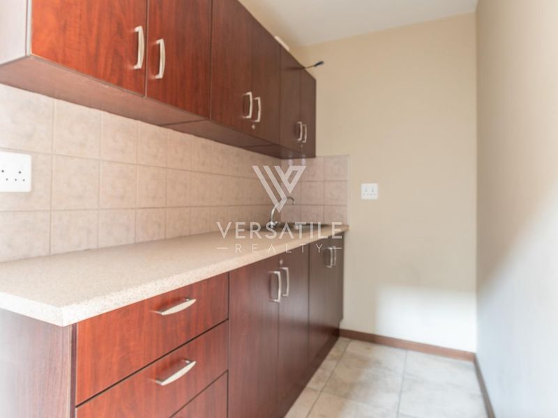 A functional scullery area featuring dark wood-look cabinetry, a neutral tiled backsplash, and a practical countertop with an integrated sink.