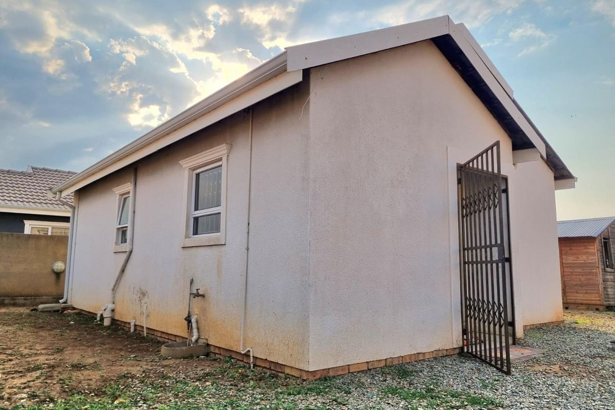 Rear exterior view of the house featuring plastered walls, security gate, and external plumbing fixtures with visible signs of exterior wall staining.