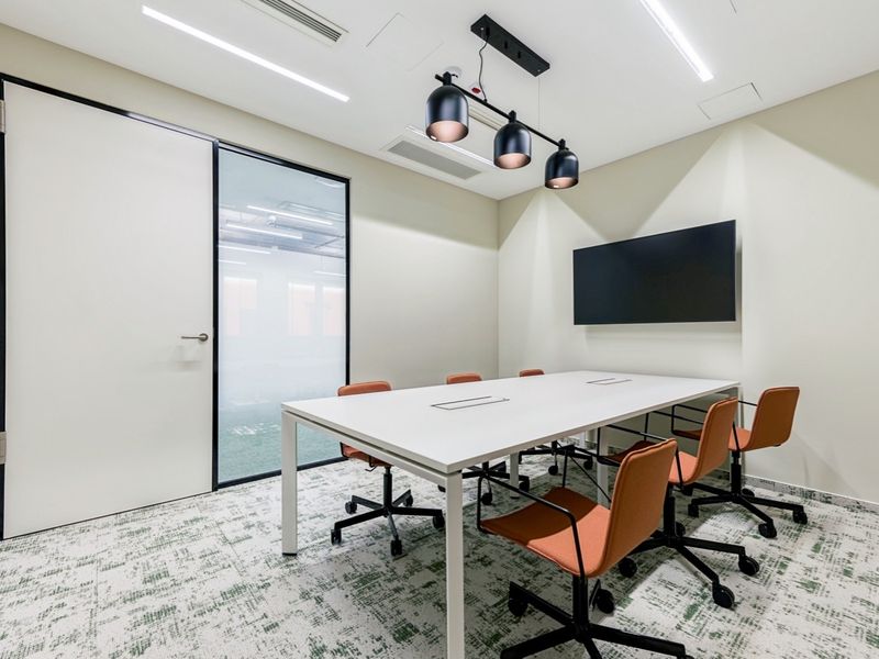 Modern professional office meeting room featuring recessed lighting, ducted air conditioning, a glass-paneled door, and a wall-mounted screen for presentations.