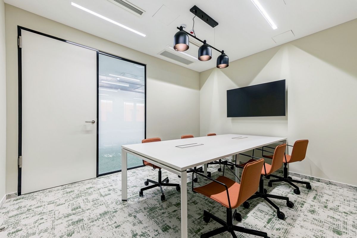 Modern professional office meeting room featuring recessed lighting, ducted air conditioning, a glass-paneled door, and a wall-mounted screen for presentations.