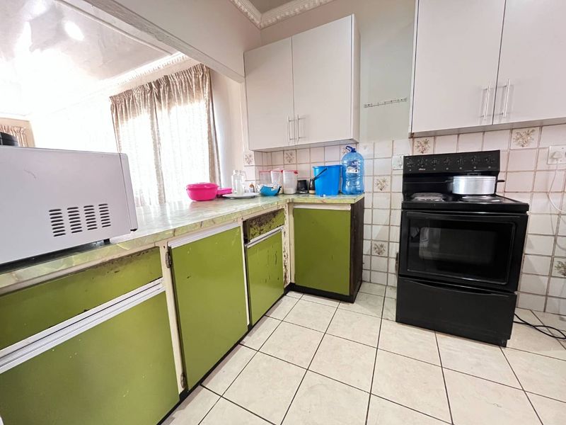 A dated kitchen featuring green lower cabinetry, white upper cabinets, tiled backsplash, and tiled flooring, offering significant potential for a modern renovation.