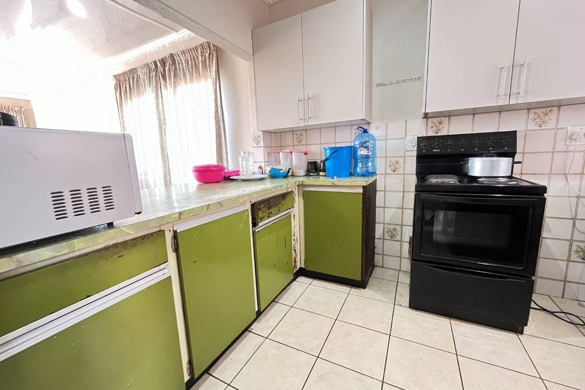 A dated kitchen featuring green lower cabinetry, white upper cabinets, tiled backsplash, and tiled flooring, offering significant potential for a modern renovation.