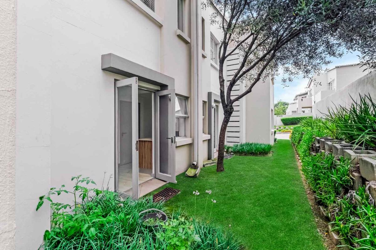 A view of the rear exterior of the house, featuring a landscaped garden, lawn, and access through glass doors.