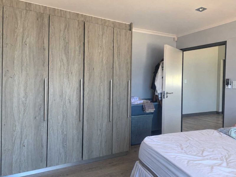 A well-maintained bedroom featuring modern wood-grain built-in cupboards and durable laminate flooring, offering ample storage and a clean, neutral aesthetic.
