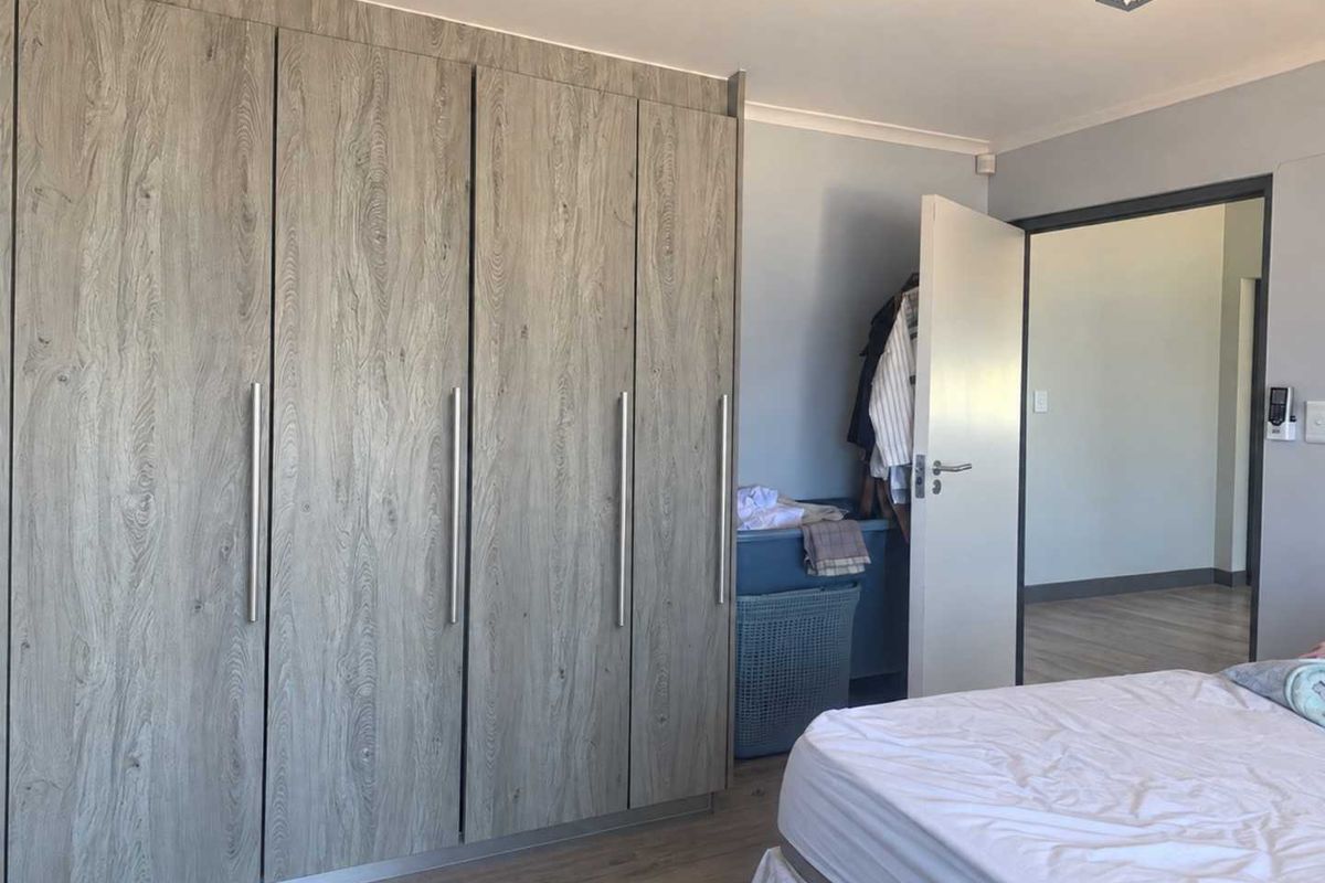 A well-maintained bedroom featuring modern wood-grain built-in cupboards and durable laminate flooring, offering ample storage and a clean, neutral aesthetic.