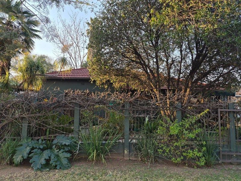 Front view of the property featuring a tiled roof, perimeter fencing, and established garden foliage.