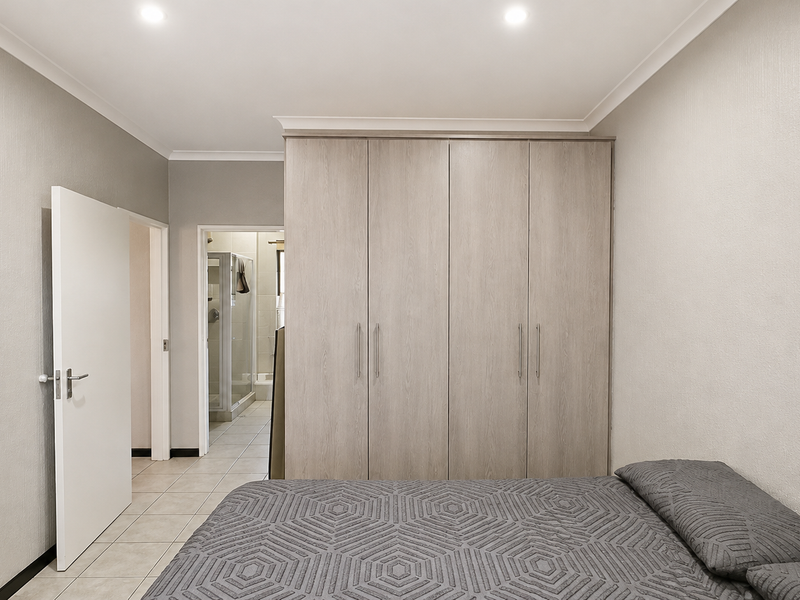 A well-maintained bedroom featuring neutral walls, tiled flooring, recessed downlights, and ample built-in cupboard storage, with an adjoining en-suite bathroom.