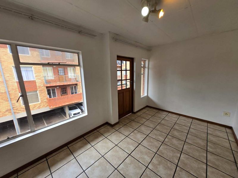 An empty living area featuring tiled flooring, large windows, and a timber door, offering a blank canvas for potential interior design updates.