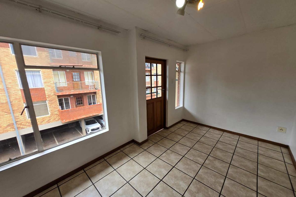 An empty living area featuring tiled flooring, large windows, and a timber door, offering a blank canvas for potential interior design updates.