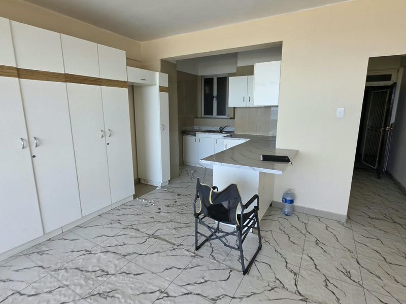 A bright kitchen featuring white built-in cabinetry, marble-look tiled flooring, and a functional breakfast bar area.