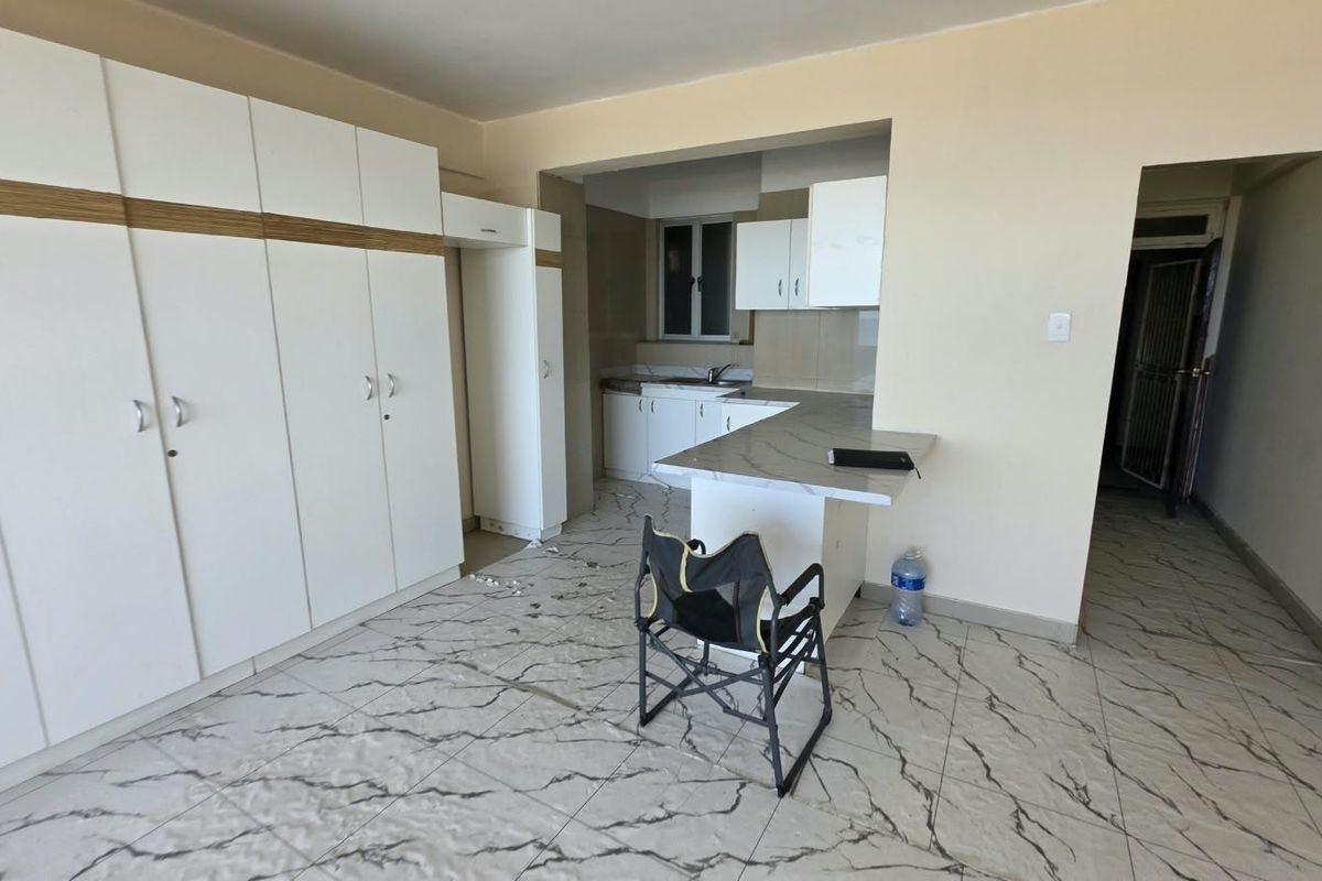 A bright kitchen featuring white built-in cabinetry, marble-look tiled flooring, and a functional breakfast bar area.