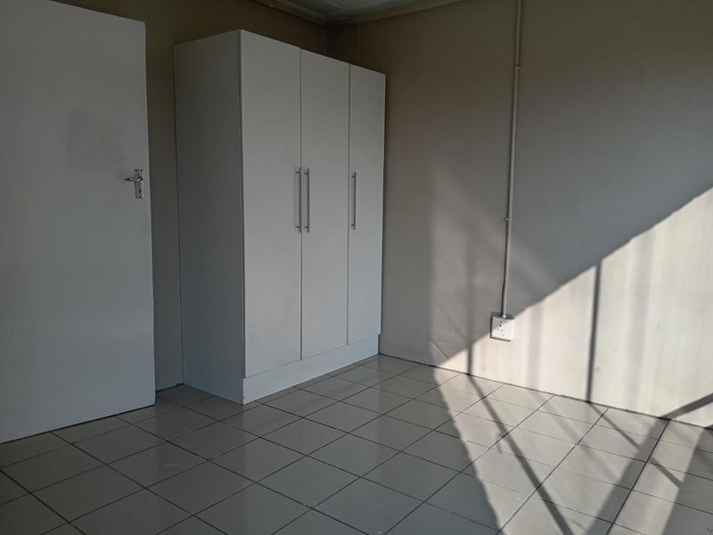 A simple, empty bedroom featuring neutral tiled flooring and a built-in white wardrobe, offering a clean and functional space ready for personalization.