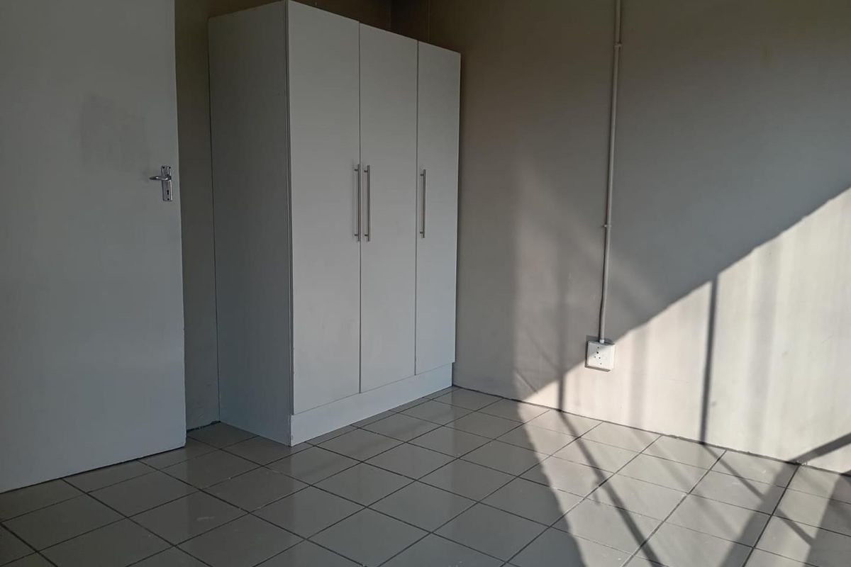A simple, empty bedroom featuring neutral tiled flooring and a built-in white wardrobe, offering a clean and functional space ready for personalization.