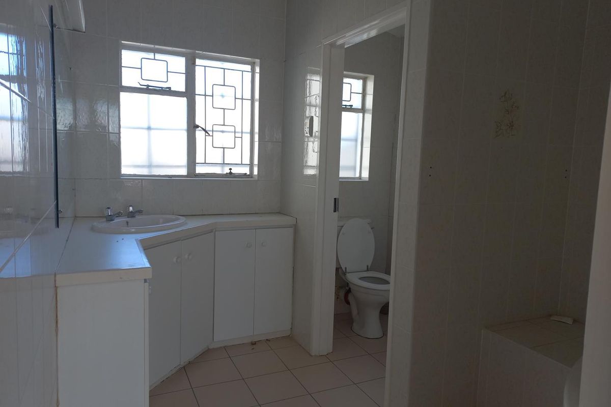A functional bathroom featuring a built-in vanity with basin, tiled walls, and a separate toilet area with natural light.