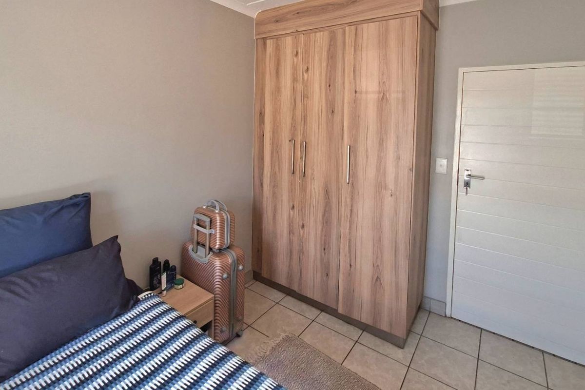 A well-maintained bedroom featuring neutral wall tones, light wood-finish built-in wardrobes, and durable tiled flooring.
