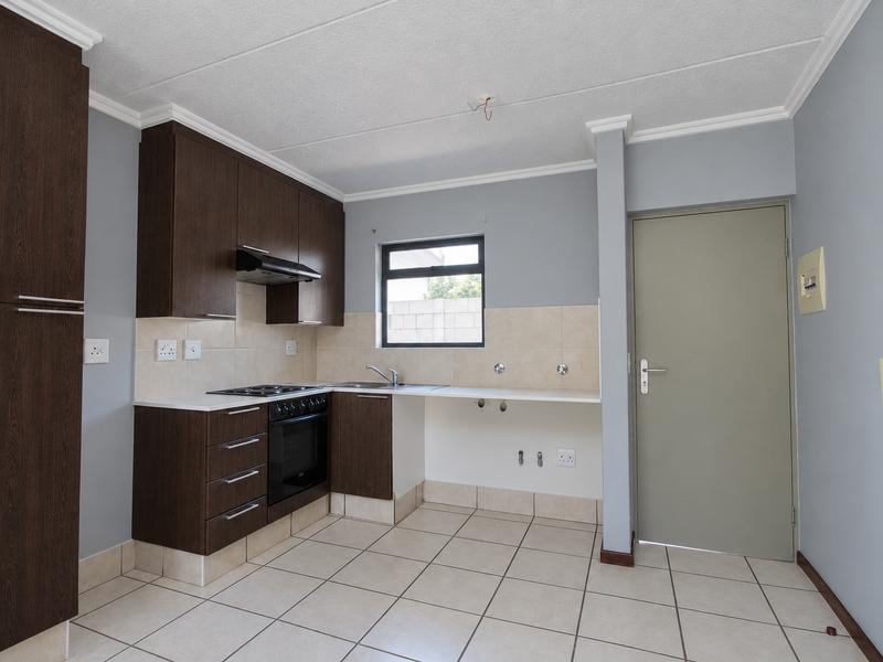 A functional kitchen featuring dark wood cabinetry, built-in oven, electric hob, and tiled flooring, offering a clean and neutral space ready for customization.