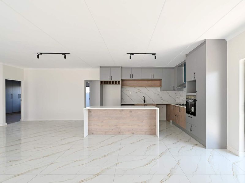 Modern open-plan kitchen featuring sleek grey and wood-tone cabinetry, a central island, marble-look tiled floors, and integrated appliances in a bright, spacious layout.