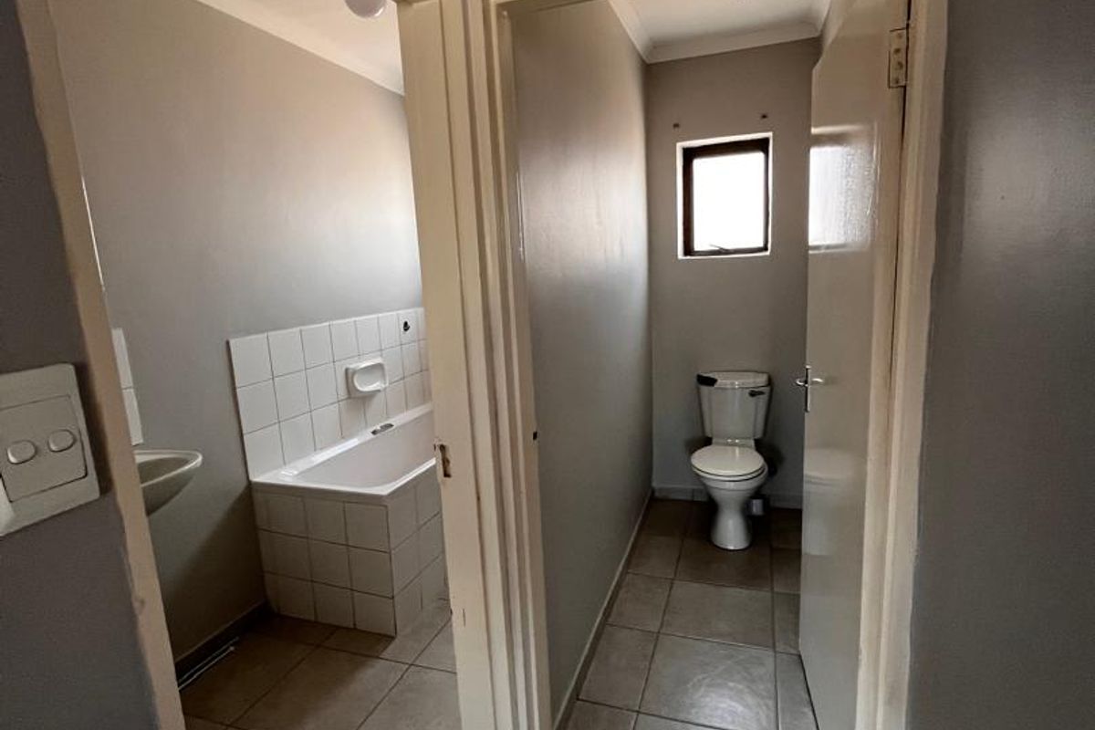 A functional bathroom featuring a tiled bathtub and a separate toilet area with neutral wall finishes and ceramic floor tiling.