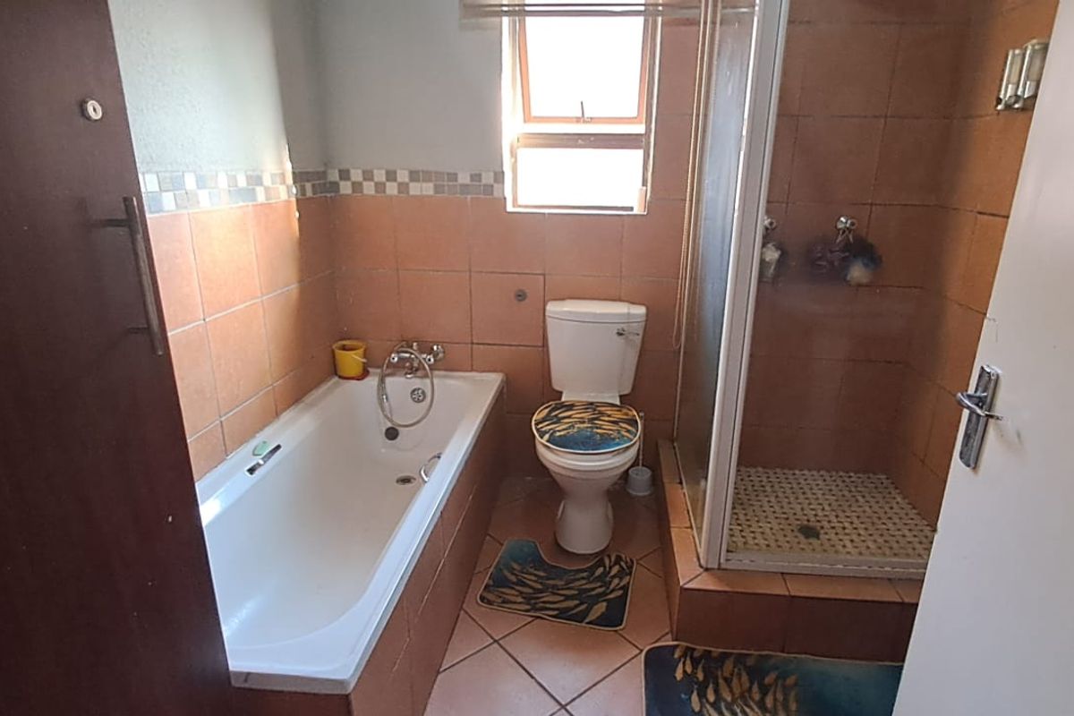 A functional bathroom featuring a built-in bathtub, a separate glass-enclosed shower, and a toilet with tiled flooring and wall accents.