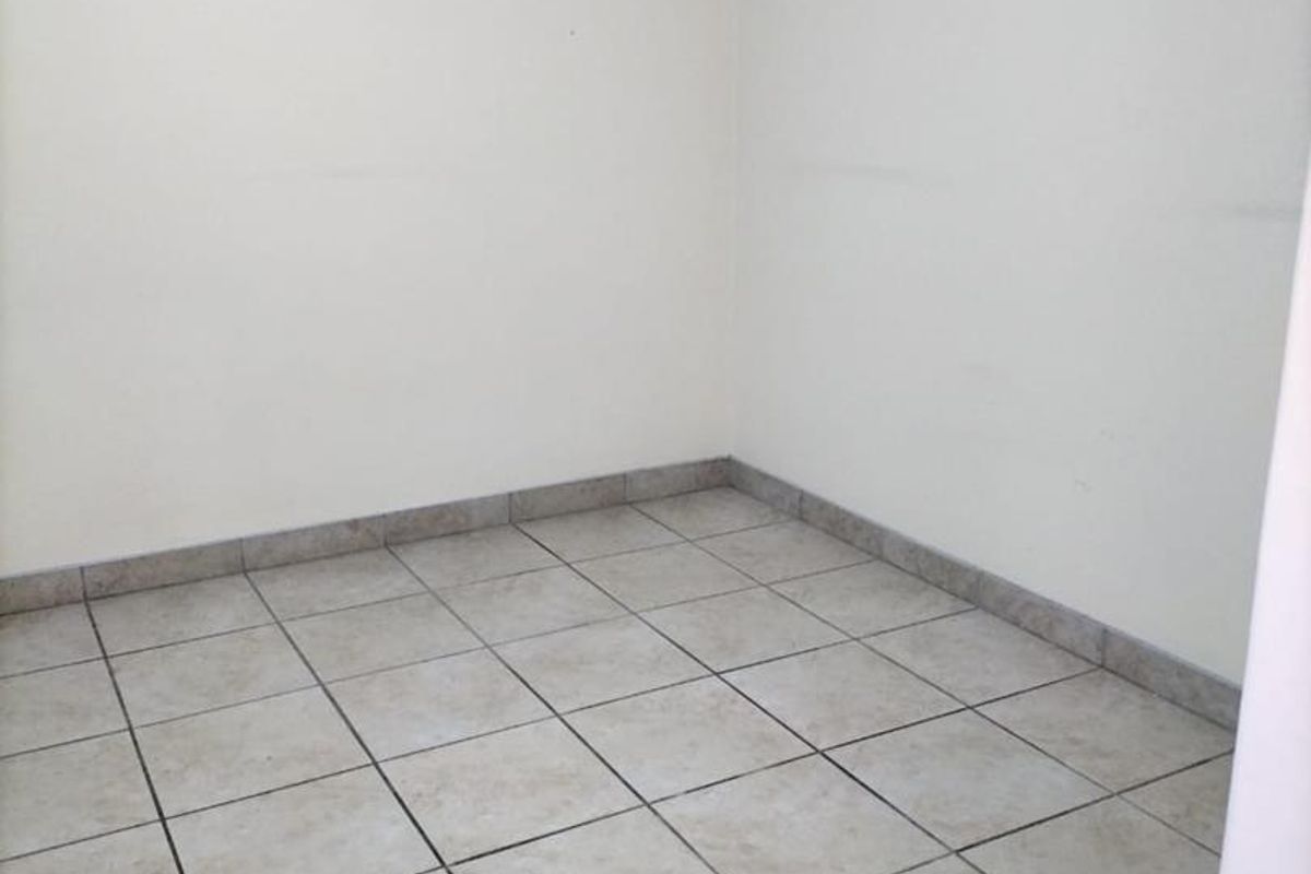 A vacant room featuring neutral ceramic floor tiles and plain white walls, offering a blank canvas for potential interior design.