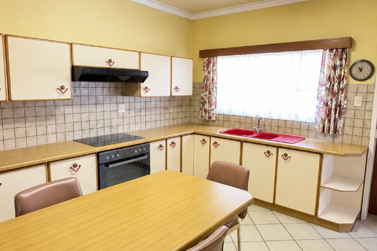 A functional kitchen featuring built-in cabinetry, an electric hob, oven, extractor fan, and a double sink with tiled splashbacks and flooring.