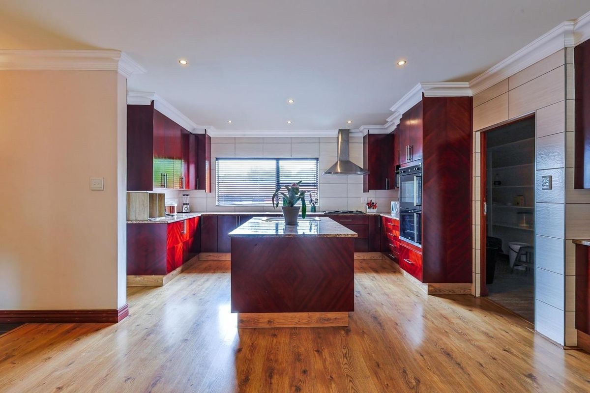 Spacious kitchen featuring dark wood cabinetry, a central island with granite countertops, built-in oven, and stainless steel extractor fan.