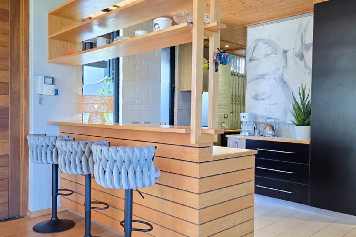 Modern kitchen featuring a timber breakfast bar with integrated shelving, black cabinetry, and warm timber ceiling finishes.