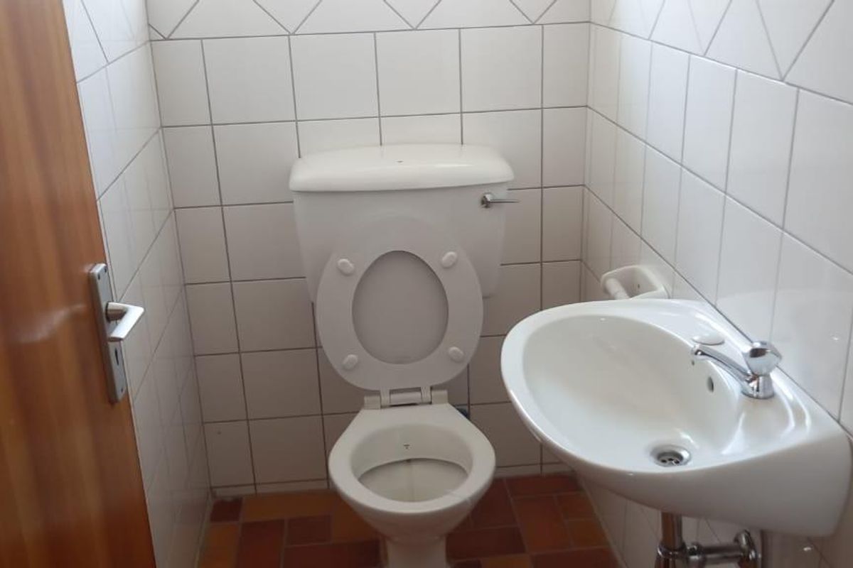 A compact office restroom featuring a standard toilet, wall-mounted basin, and full-height white ceramic wall tiling.