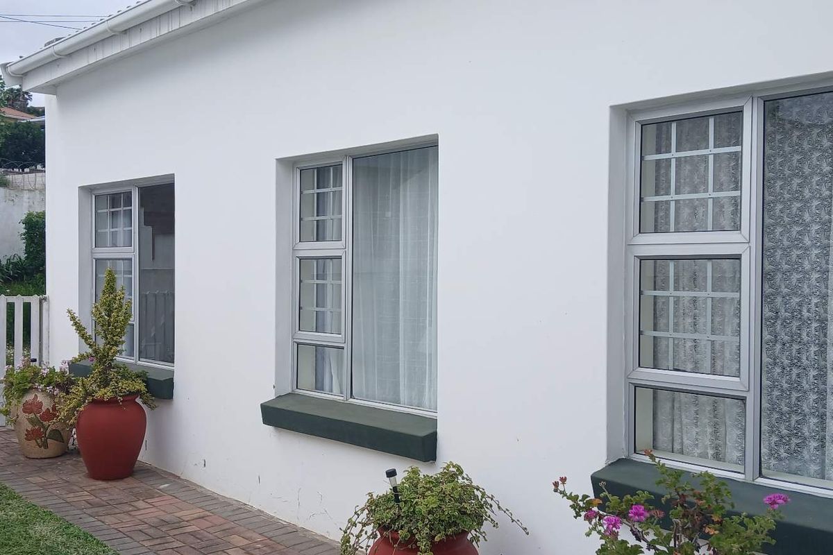 A view of the rear exterior wall featuring white painted masonry, aluminium window frames with security bars, and a paved garden walkway.