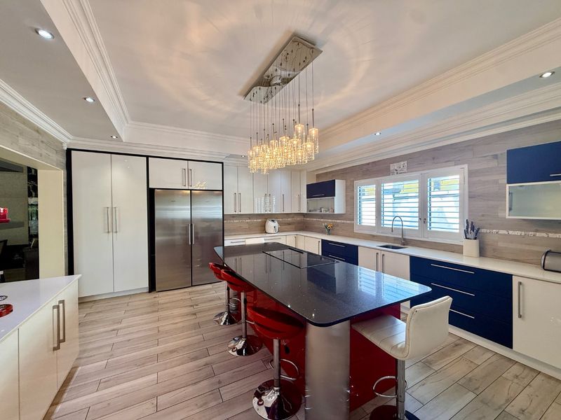 Modern kitchen featuring a large central island with stone countertops, high-gloss cabinetry, integrated appliances, and stylish pendant lighting.