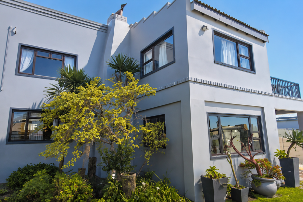 A well-maintained two-story residential exterior featuring a modern grey facade, aluminium window frames, a chimney, and an upper-level balcony.
