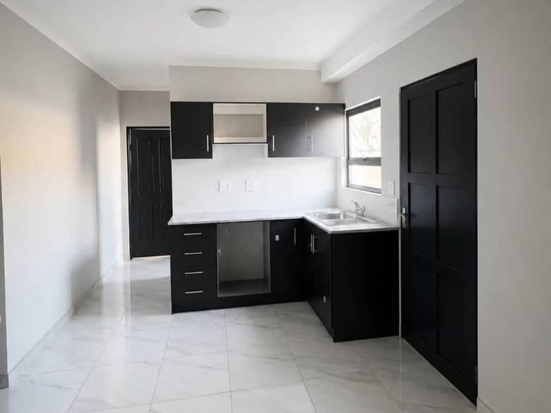 A modern, minimalist kitchen featuring sleek black cabinetry, marble-look tiled flooring, and a built-in extractor fan in a clean, neutral space.