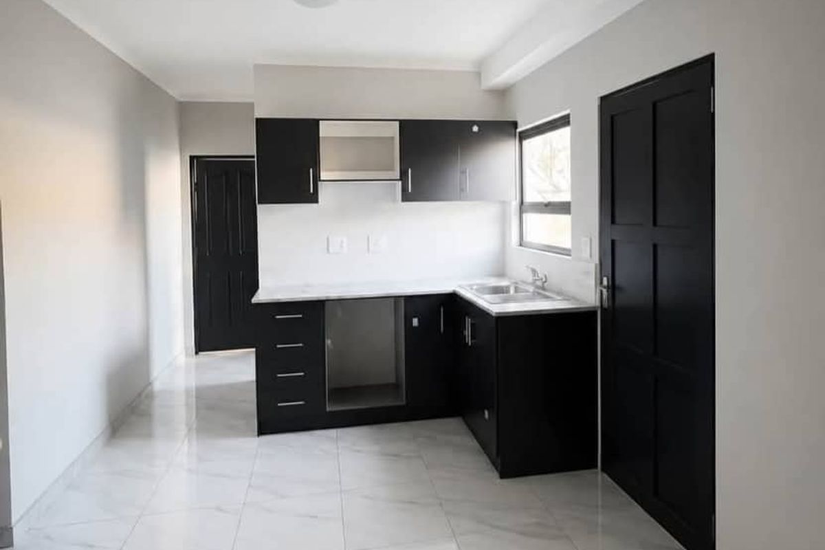 A modern, minimalist kitchen featuring sleek black cabinetry, marble-look tiled flooring, and a built-in extractor fan in a clean, neutral space.
