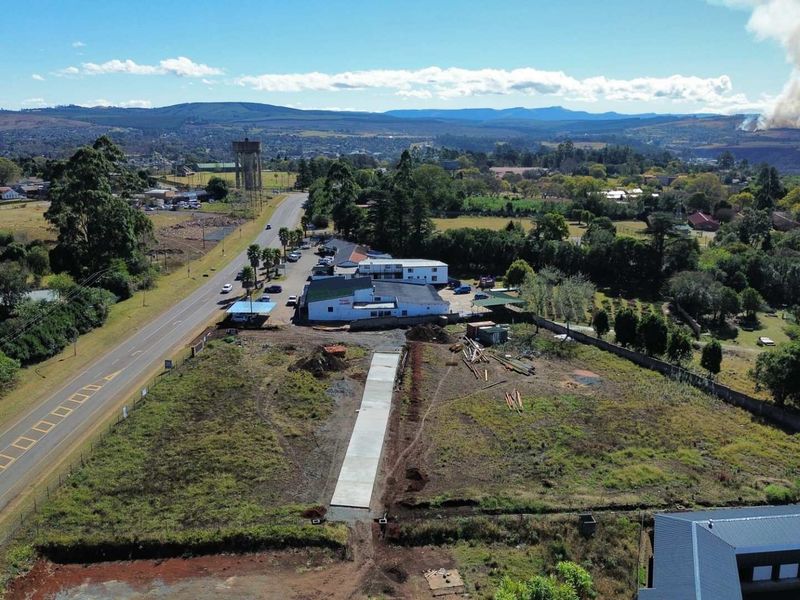 Aerial view of a vacant commercial land parcel featuring a newly laid concrete driveway, perimeter fencing, and direct access to the main road.