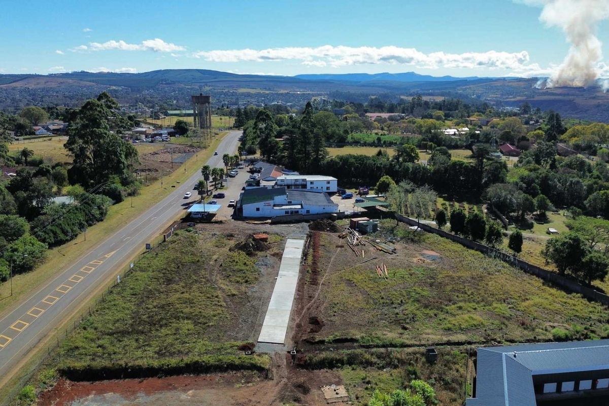 Aerial view of a vacant commercial land parcel featuring a newly laid concrete driveway, perimeter fencing, and direct access to the main road.