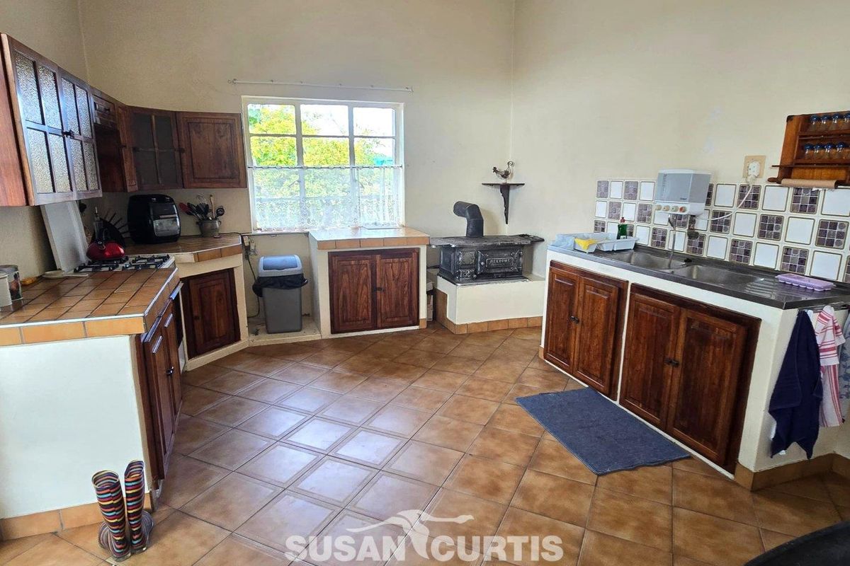 A rustic farm-style kitchen featuring wooden cabinetry, tiled countertops, a built-in wood-burning stove, and a double basin sink.