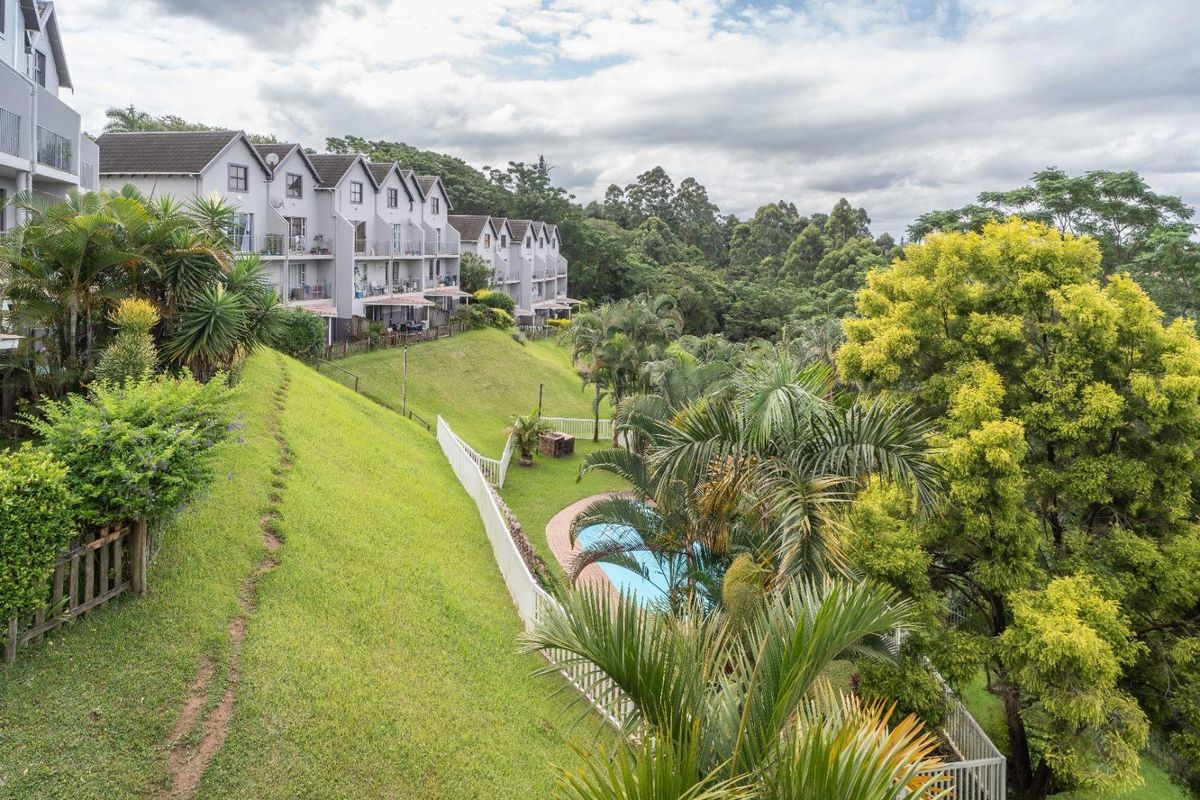 Elevated view of the rear apartment complex featuring a communal swimming pool, landscaped garden areas, and established trees.